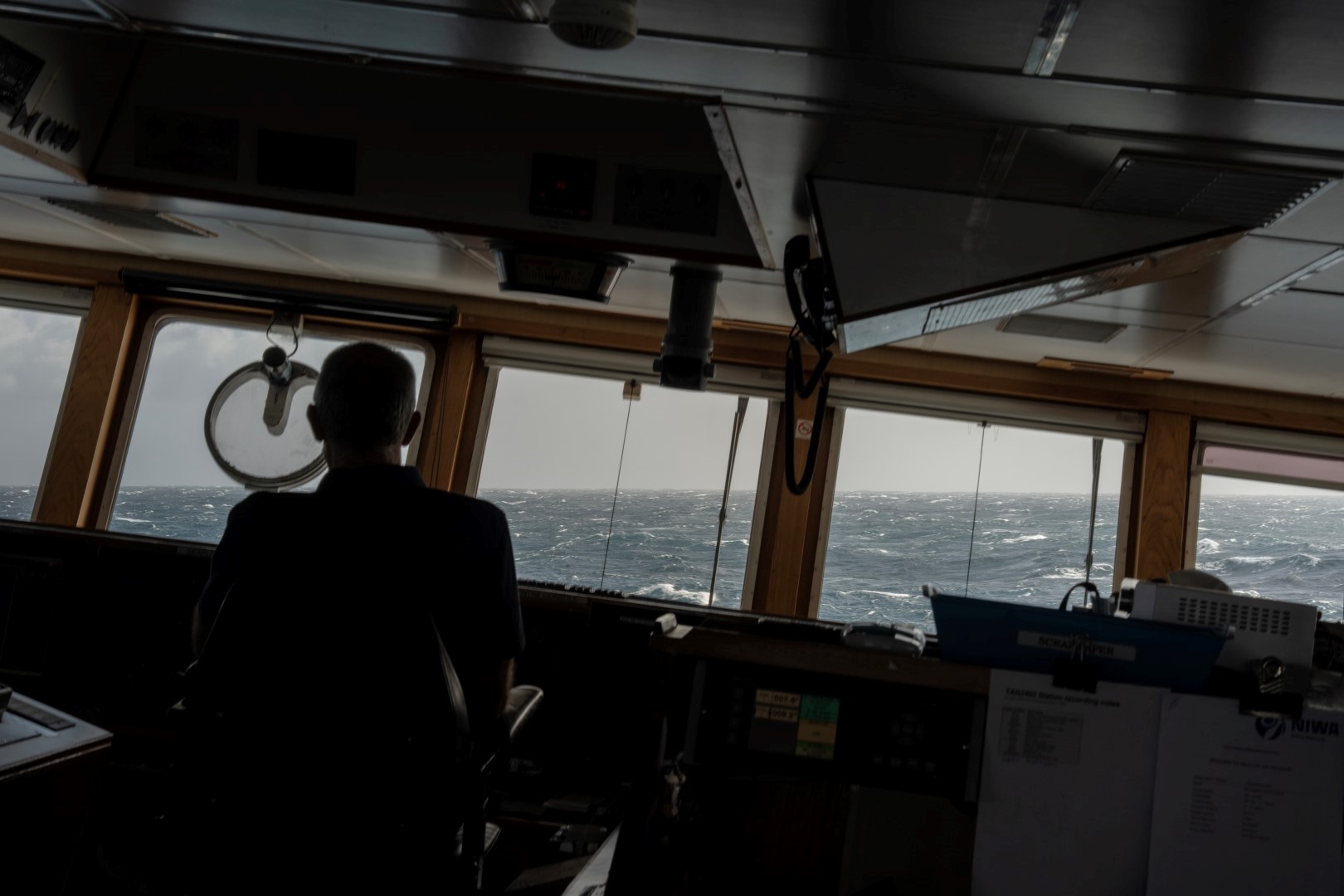 Ship captain looking at rough seas through windows on the bridge of Research Vessel Tangaroa.