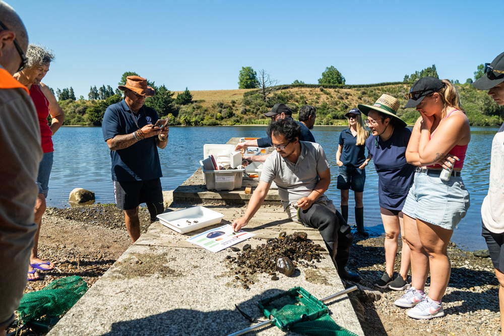 Poto Davies (Ngāti Koroki Kahukura), Niketi Toataua (NIWA Pou Arahi), Associate Professor Dr Yu Cao (Wuhan Botanic Garden, CAS), Deborah Hofstra (NIWA Principal Scientist), Merekara Warrington (Ngāti Koroki Kahukura), and Sidney Robcke (University of Waikato) at a gold clam hui. Bob's Landing, Waikato.